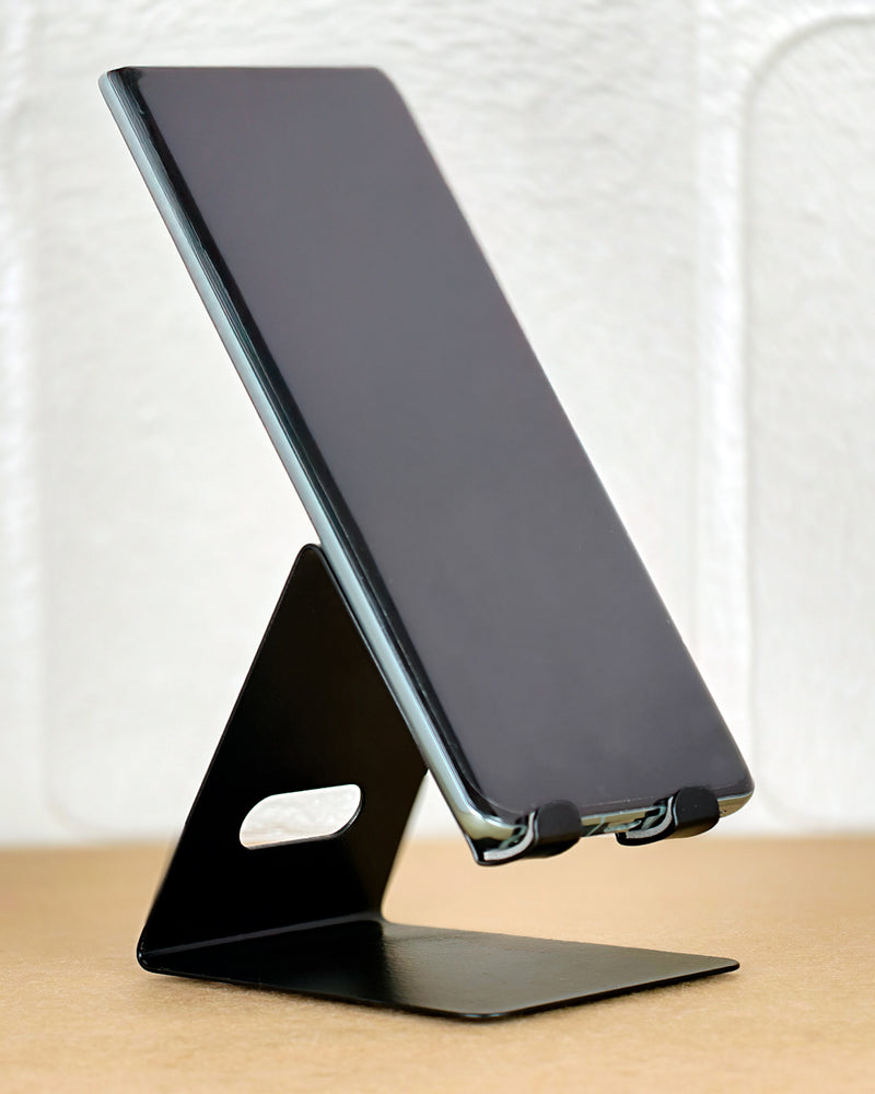 Black phone stand holding a smartphone on a wooden surface with a white background