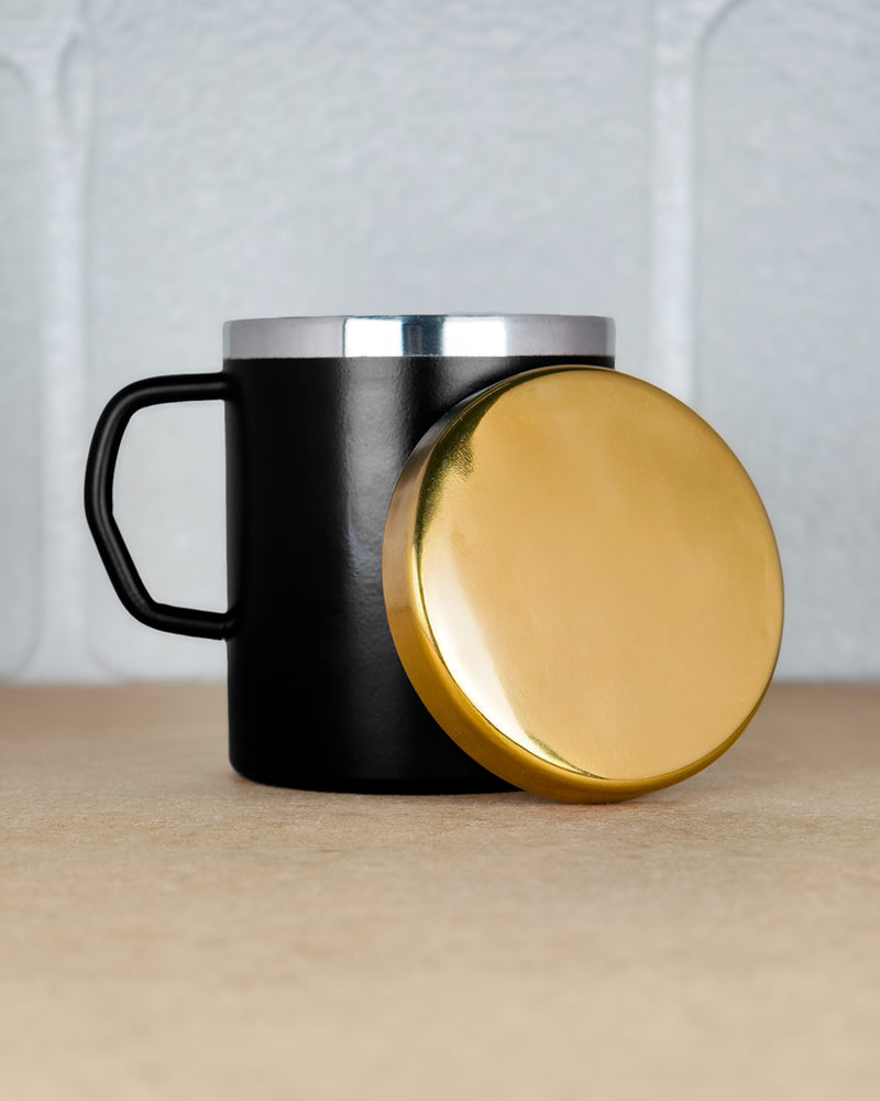 Black mug with gold lid and silver top on a neutral background