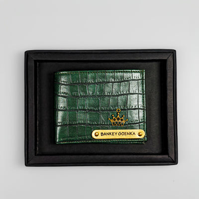A green, crocodile-patterned leather wallet with a personalized name plate, displayed in a black frame.