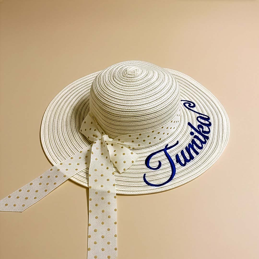 Beige straw hat with a polka dot ribbon and 'Junko' embroidery on a beige background