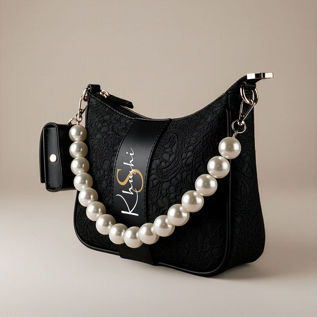 Black SLING BAG with a pearl necklace draped over it on a beige background