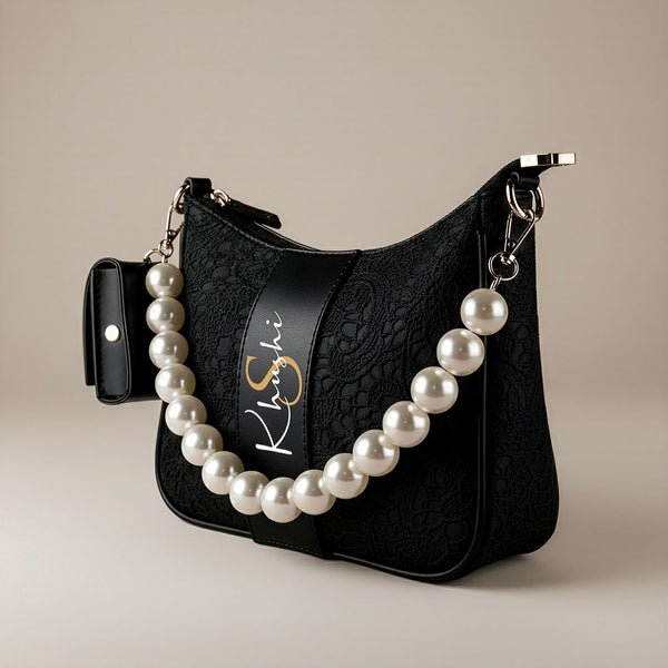 Black SLING BAG with a pearl necklace draped over it on a beige background