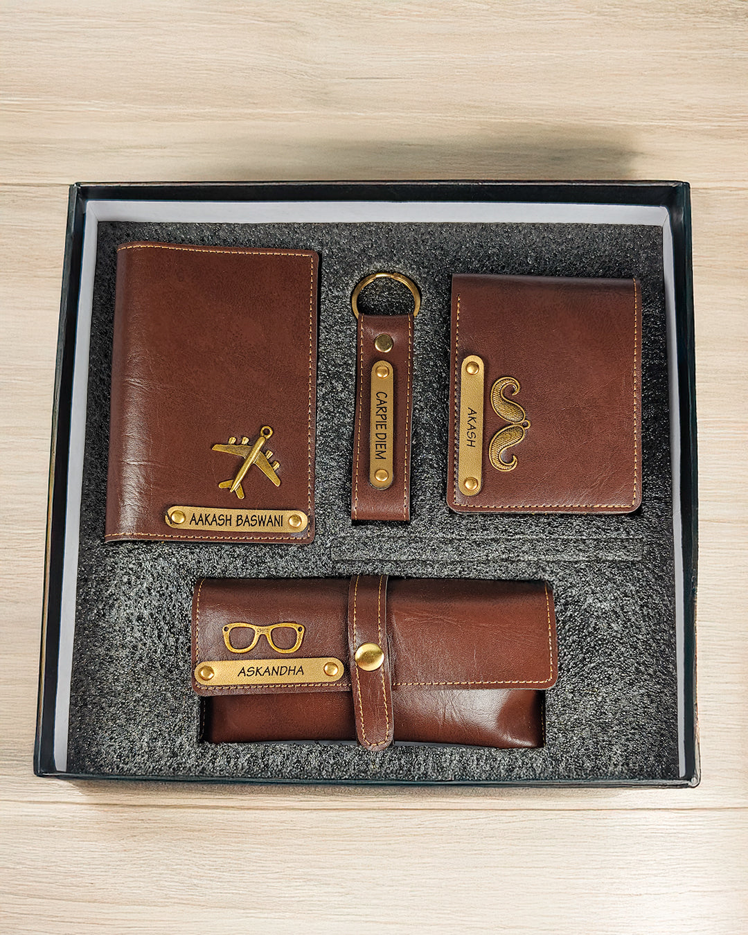 Set of brown leather wallets and keychain with gold accents in a box on a wooden surface