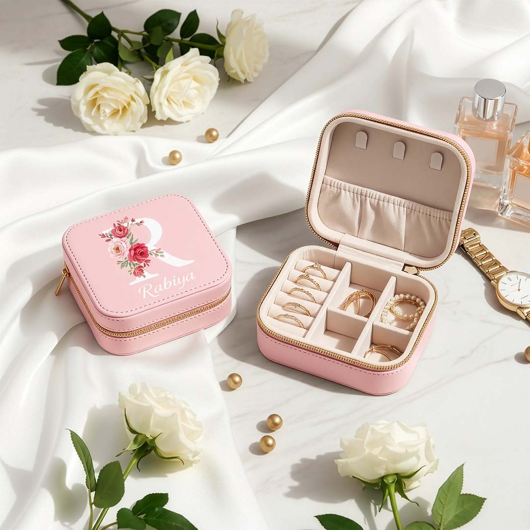Pink jewelry box with floral design on a white fabric background with flowers and a watch.