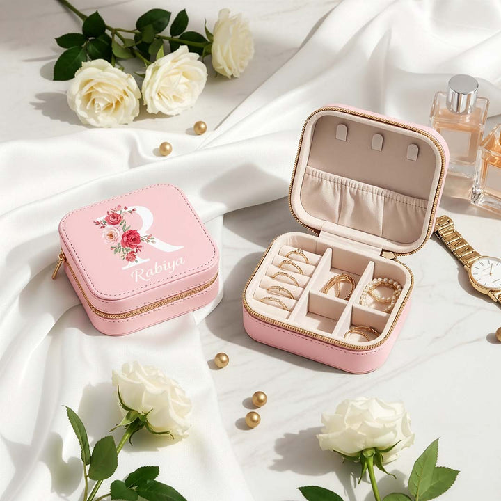 Pink jewelry box with floral design on a white fabric background with flowers and a watch.