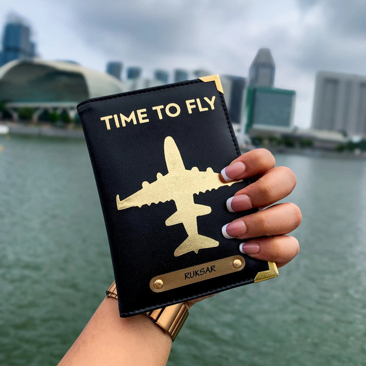 A hand holding a black passport cover with gold aviation-inspired design and text &