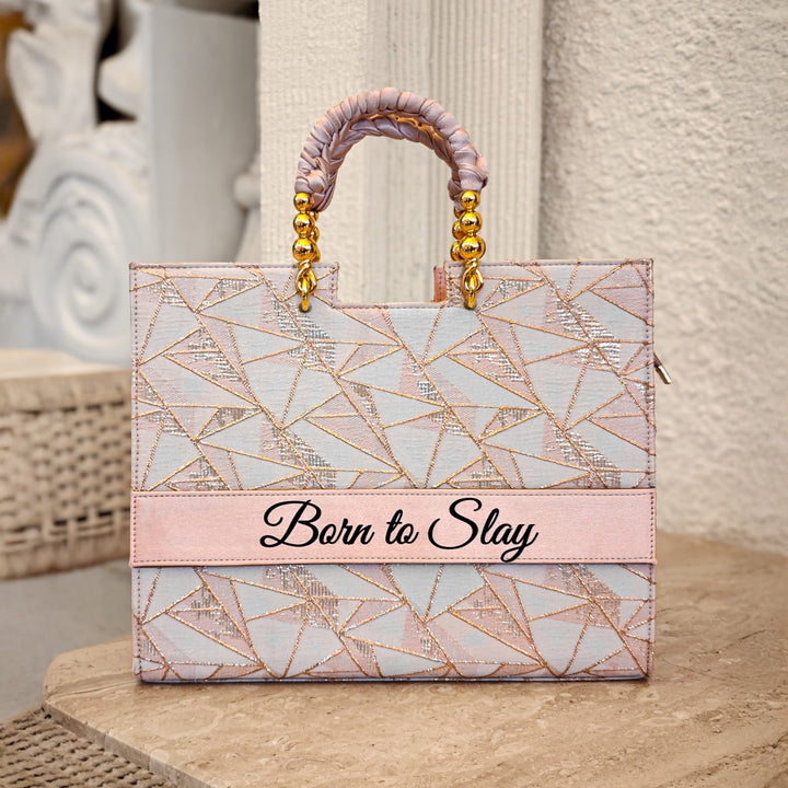A tote bag with a geometric pattern in pink tones and a gold-plated handle, placed on a marble surface with the text &