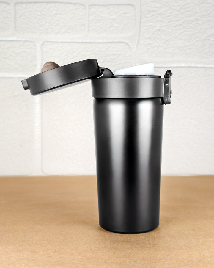 Black trash can with a wooden lid on a wooden surface against a white tiled wall.