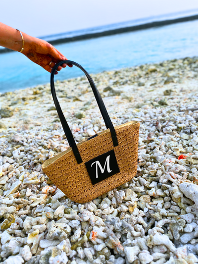Personalised Brown Cane Beach Bag - Luxe Edition on the Maldives beach surrounded by pebbles