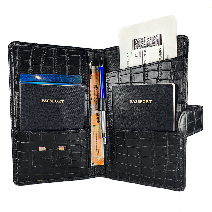 Black crocodile-patterned passport holder with two passport slots, a pen, and other travel documents on a white background.