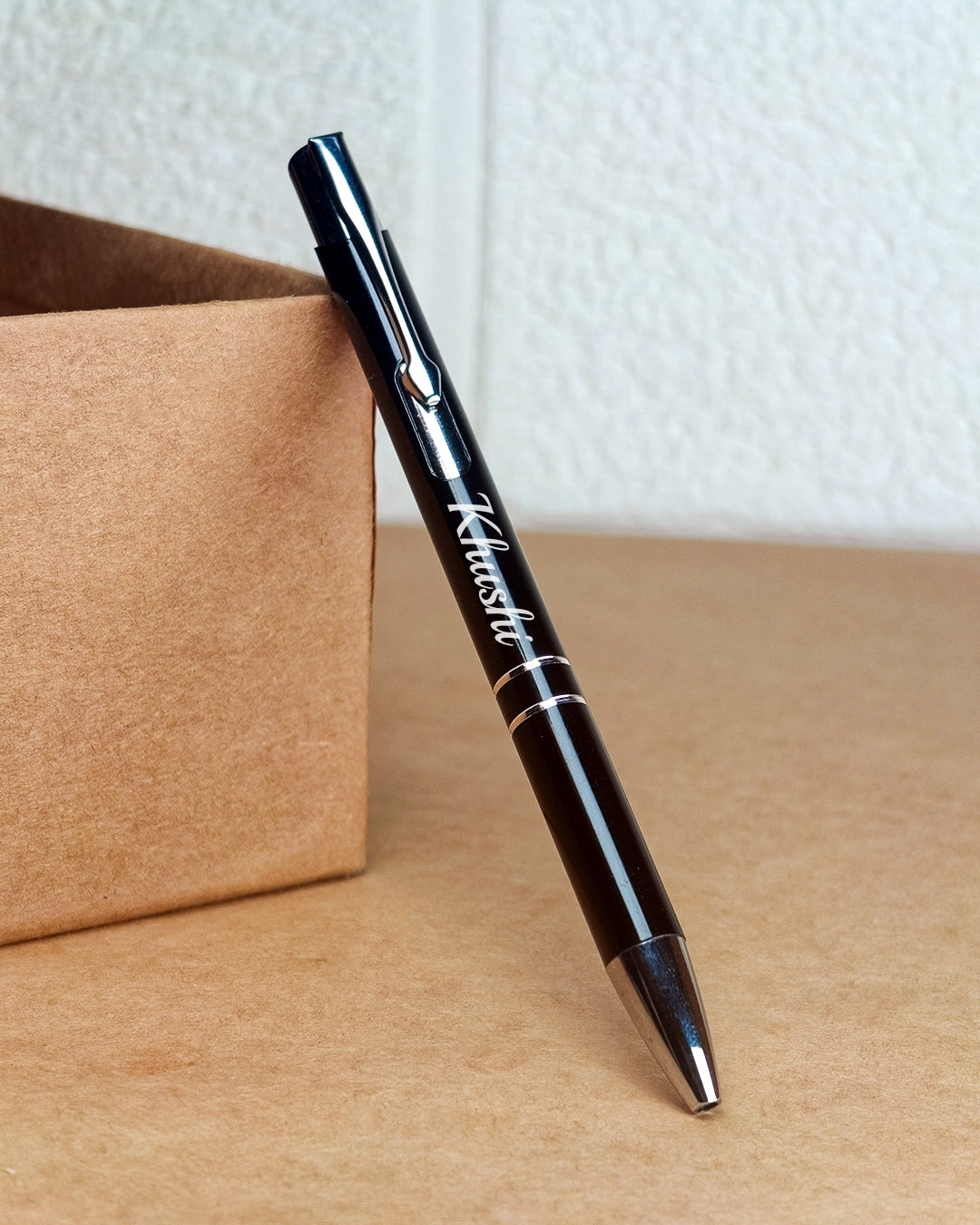 Black pen with silver accents on a wooden surface next to a cardboard box.