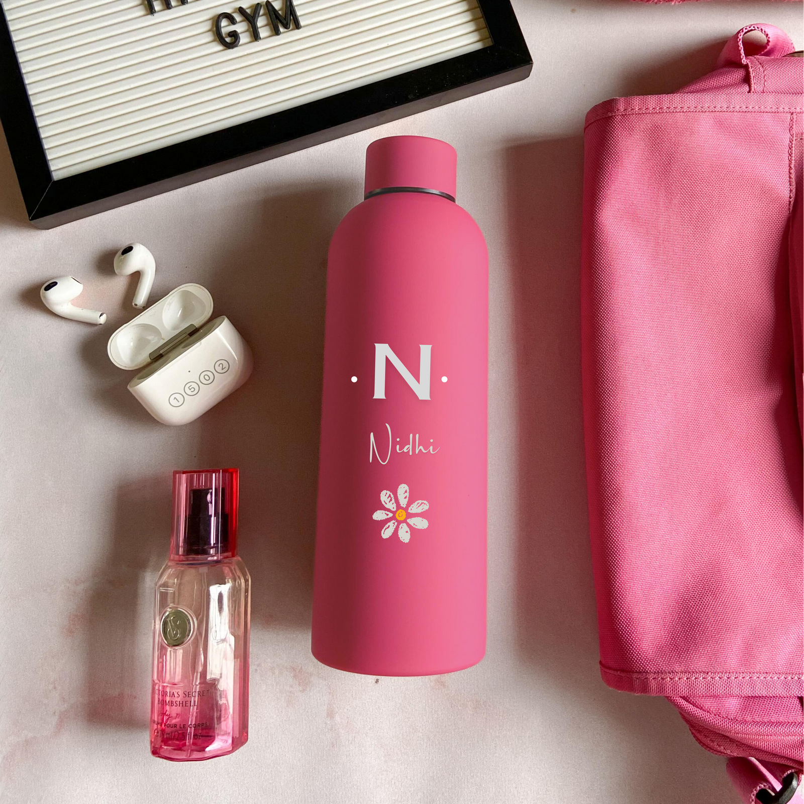 A hot pink stainless steel water bottle with custom engraving, displayed alongside gym accessories, indicating the bottle is personalized and eco-friendly.