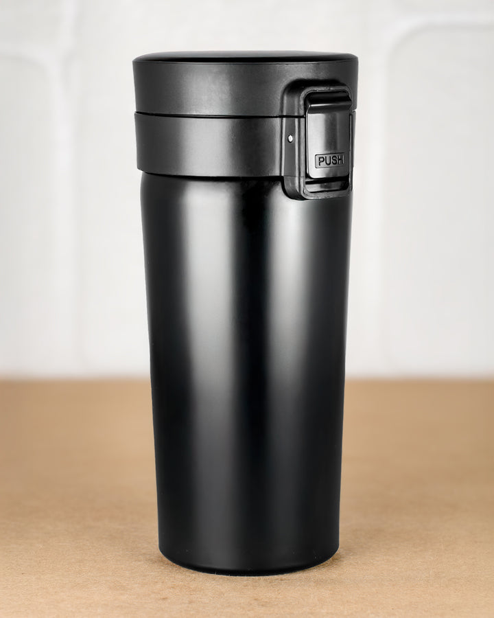 Black travel mug with push lid on a beige surface