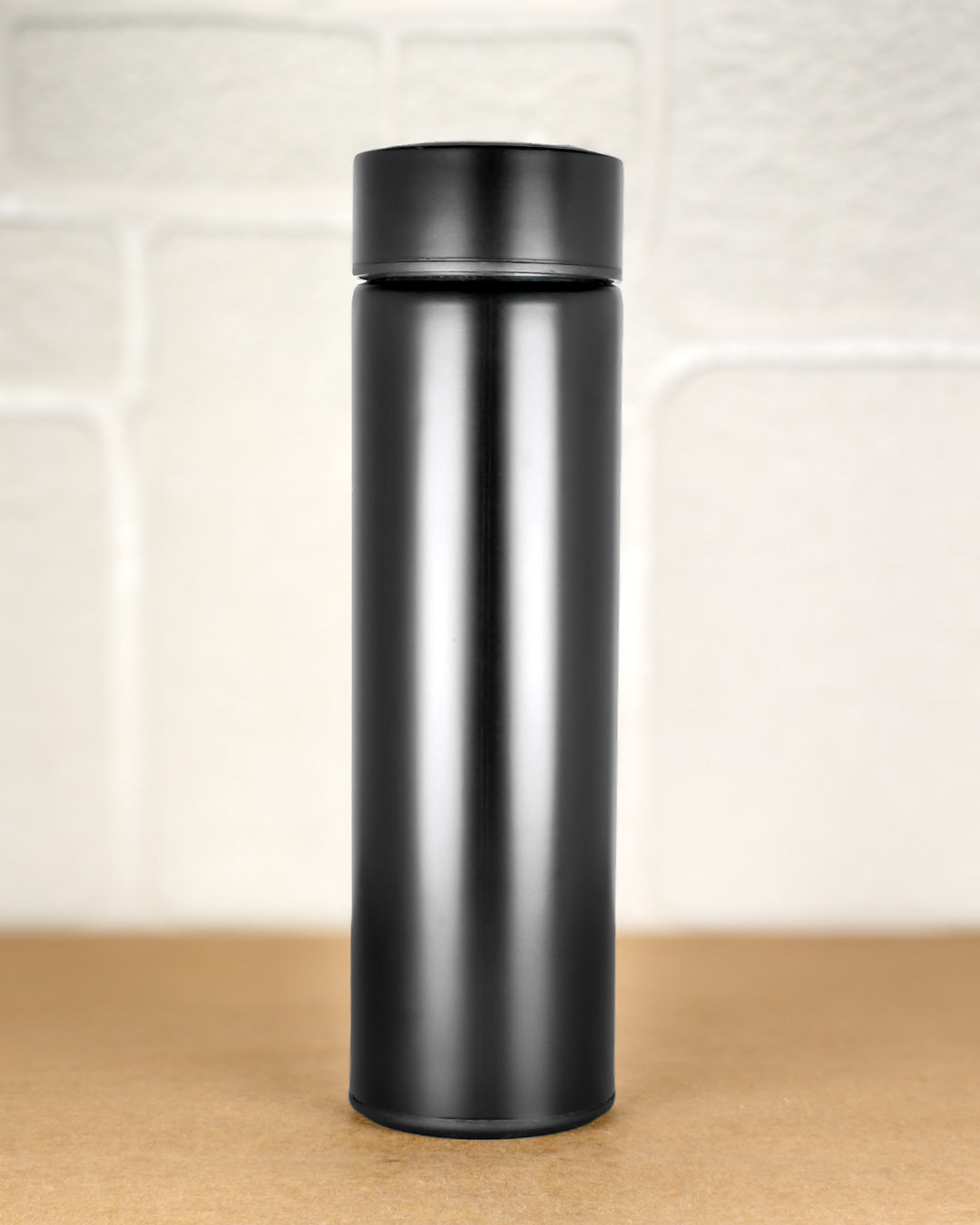 Black insulated bottle on a wooden surface with a light-colored tile background