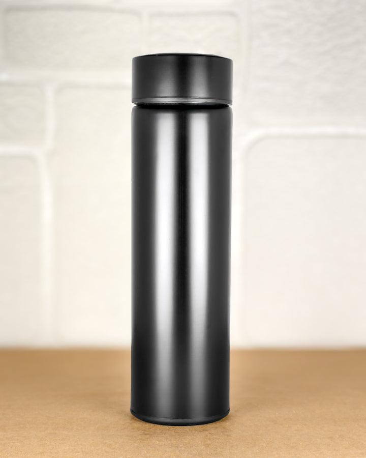 Black insulated bottle on a wooden surface with a light-colored tile background