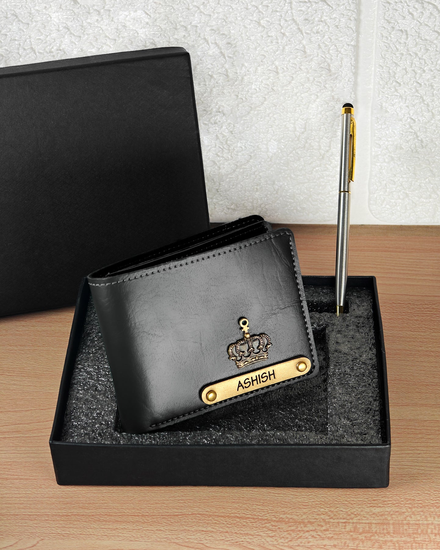 Black leather wallet with gold accents and 'ASHISH' branding on a wooden surface.