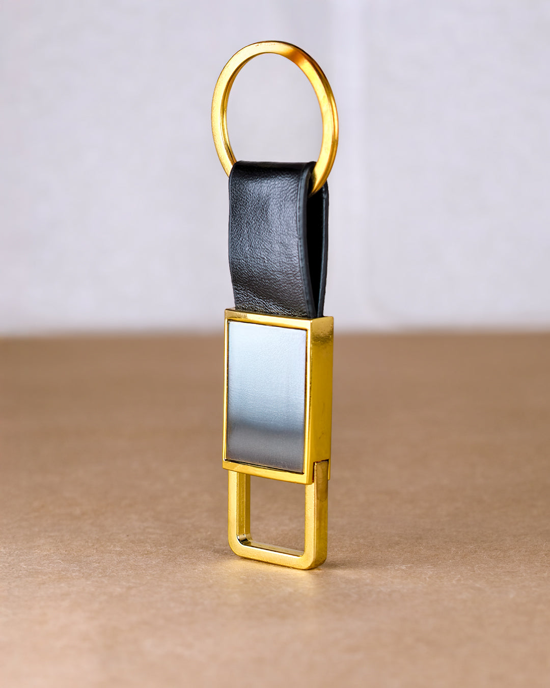 Gold keychain with black leather strap on a beige surface
