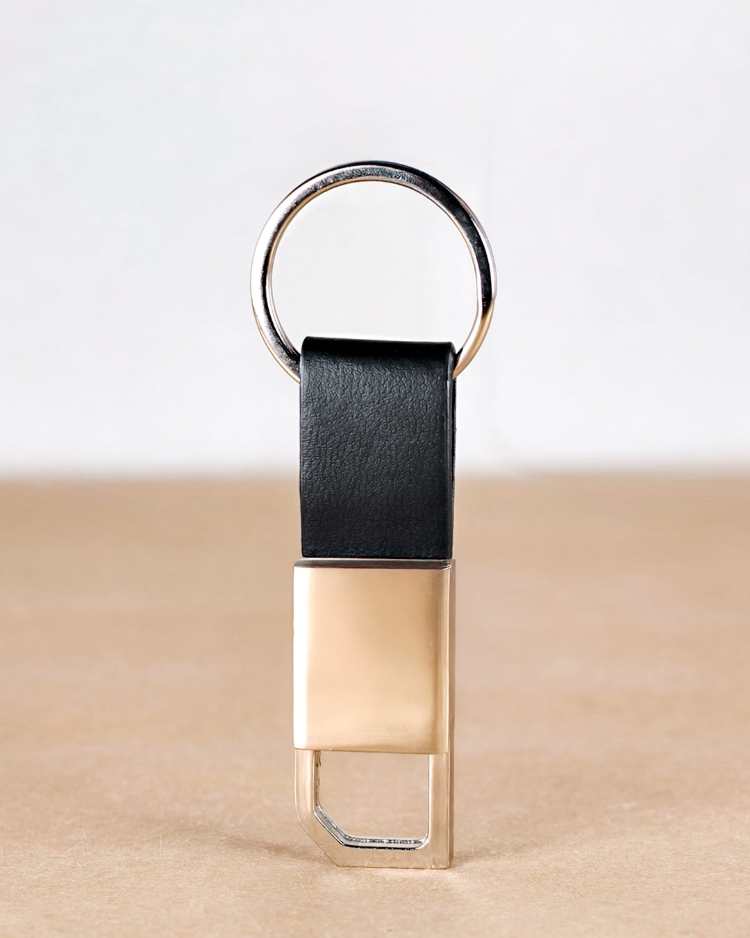 Gold keychain with black leather strap on a beige surface
