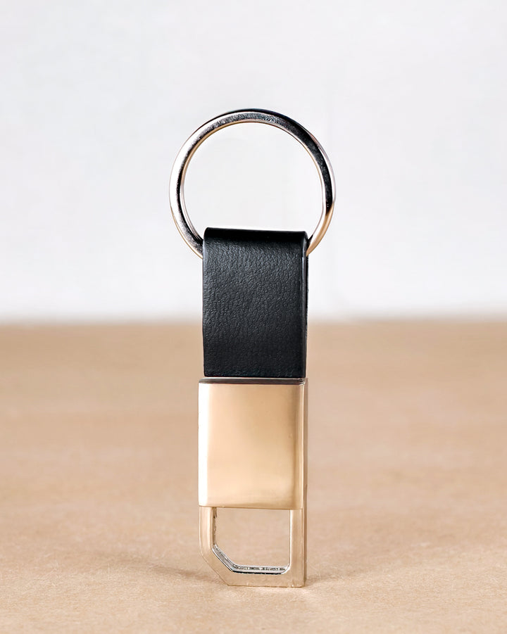 Gold keychain with black leather strap on a beige surface