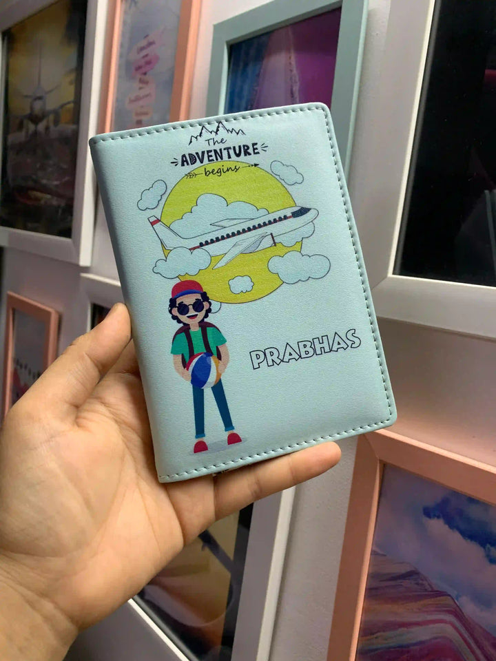 A hand holding a light blue passport cover featuring a colorful cartoon illustration of a traveler under a yellow sun with the text &