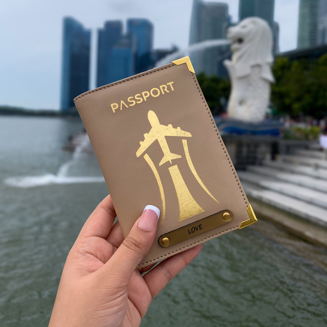 A hand holding a black passport cover with gold aviation-inspired design and text &