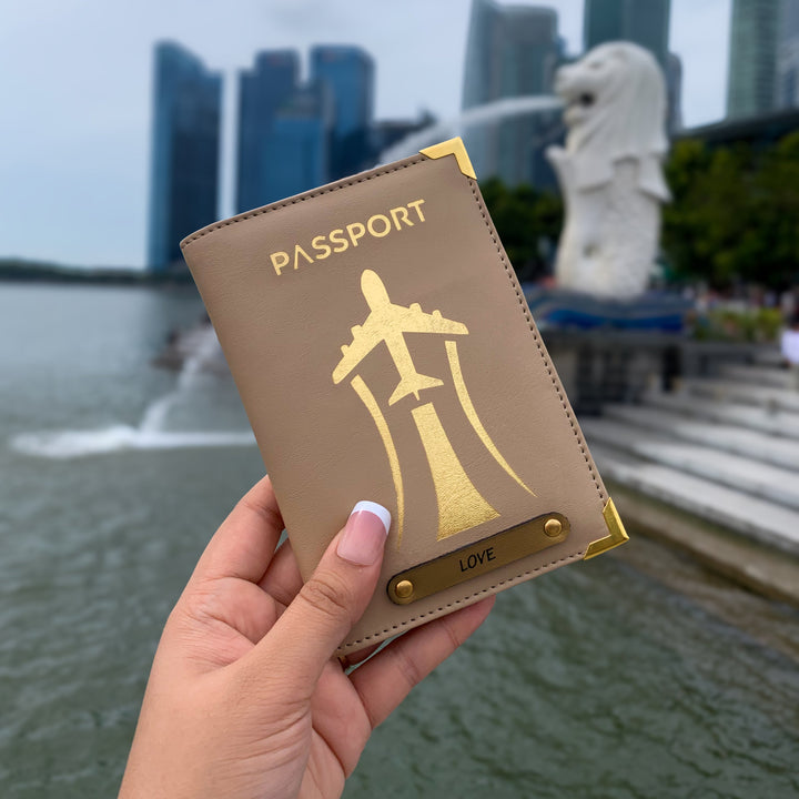 A hand holding a black passport cover with gold aviation-inspired design and text &