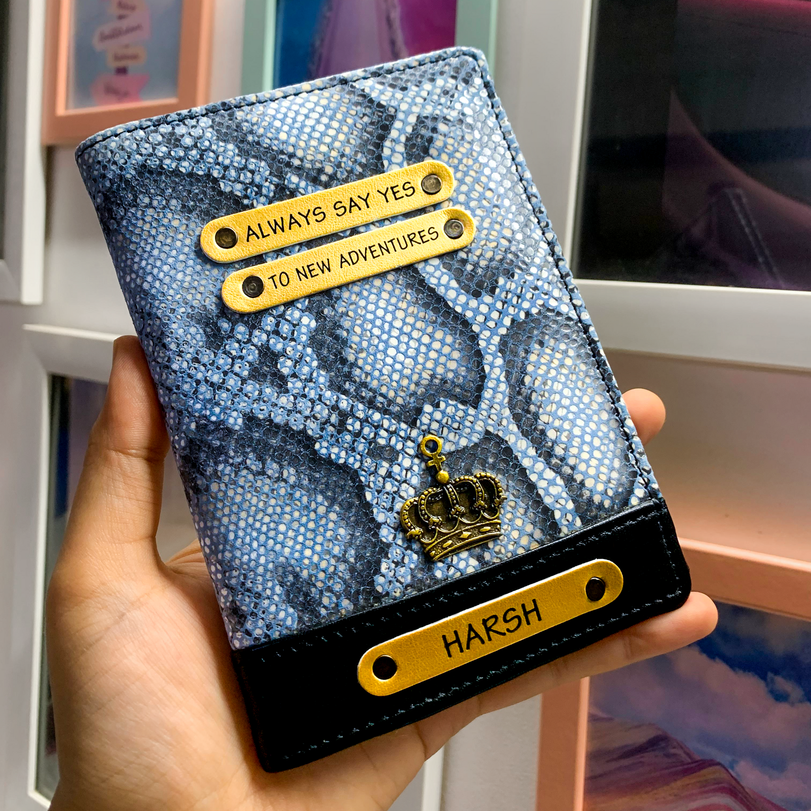 A personalized passport cover in blue with a snake skin pattern. It features a name tag and charm, and is displayed in a vertical orientation.