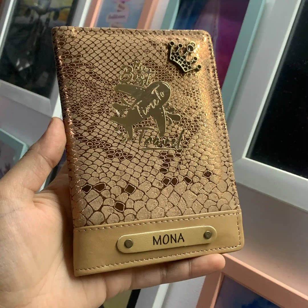 A hand holding a personalized snakeskin-patterned passport cover in a warm tan color. The cover features an embossed design with a crown, the phrase &