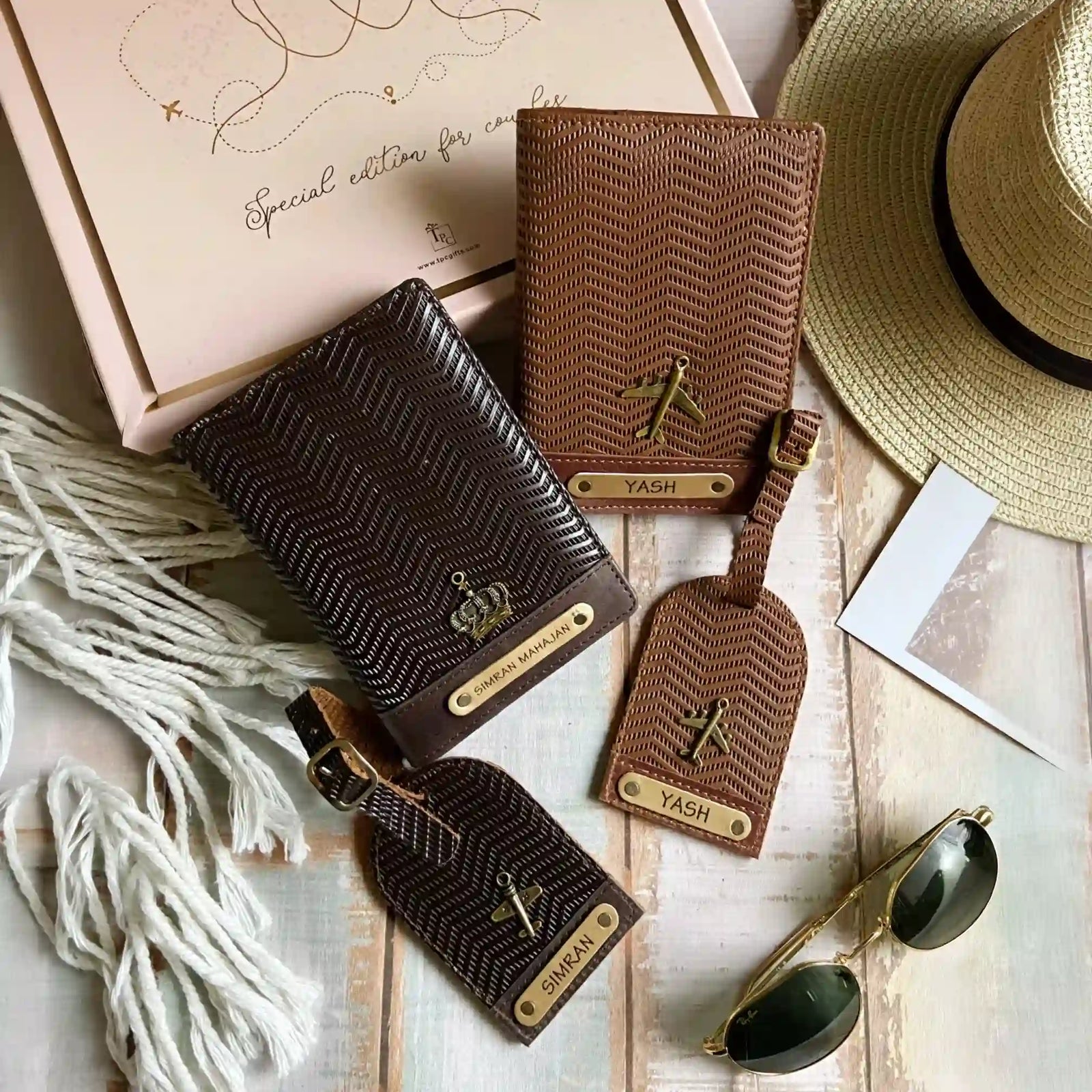 A set of couple passport covers and luggage tags with a wavy texture design in light brown and dark brown colors, displayed alongside travel-related items like a hat and sunglasses hand with the word 'YASH' embossed on it, against a backdrop of a passport, visa, and sunglasses -TPC Gifts