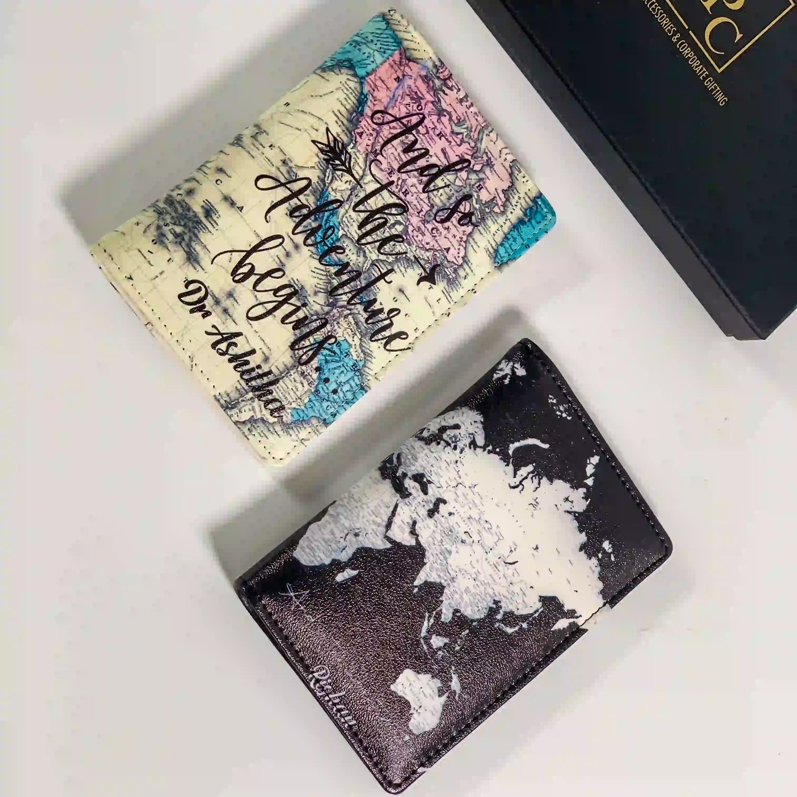Couple print map passport covers one has a cream base with a colorful map print and cursive text; the other has a black-and-white world map print  hand by TPC Gifts. O