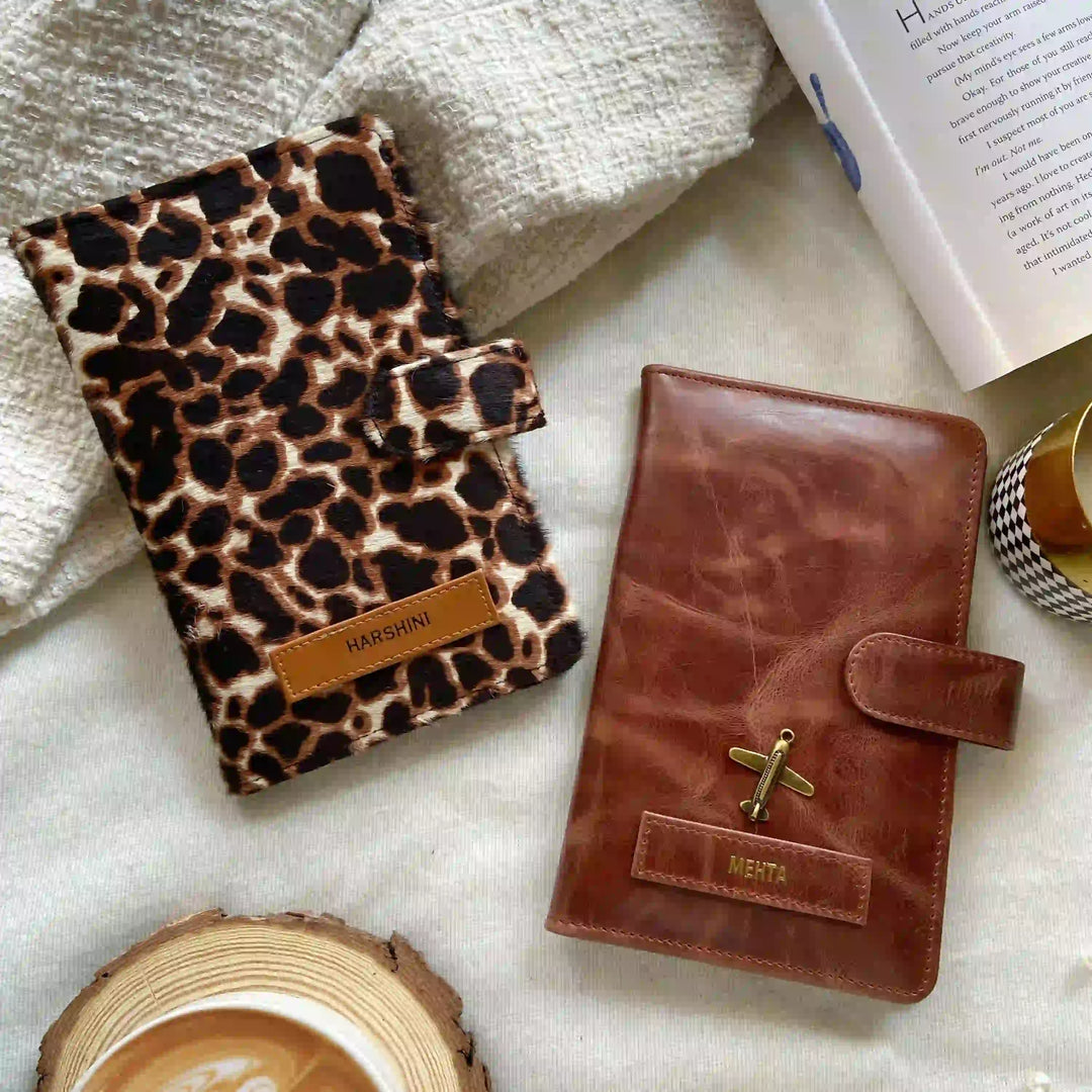 Two personalized planner covers styled on a textured white fabric background with lifestyle props. One cover features a brown and black leopard print pattern with a tan leather tab labeled &