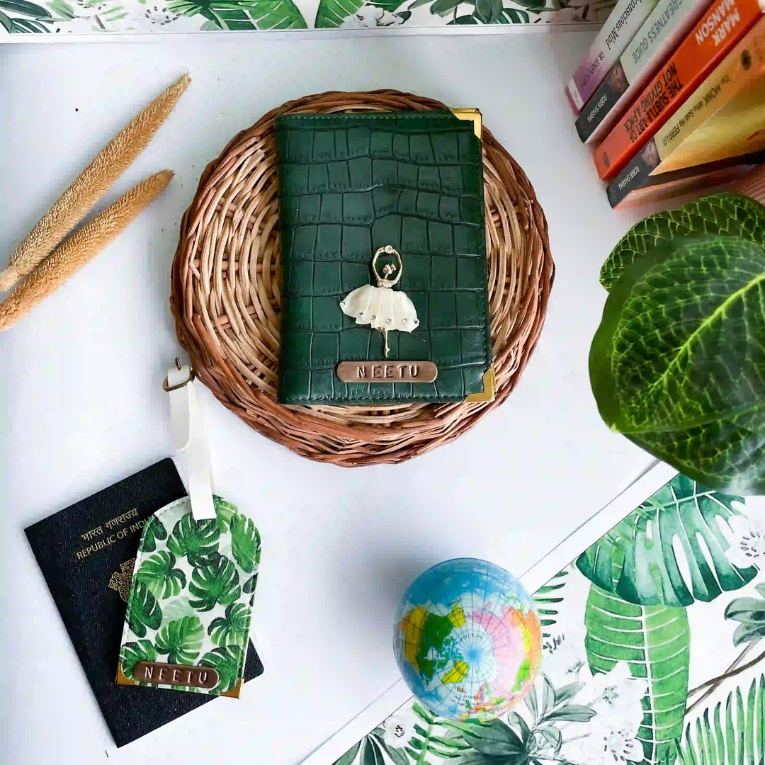 A dark green crocodile-embossed passport cover with a white ballerina charm and a gold &