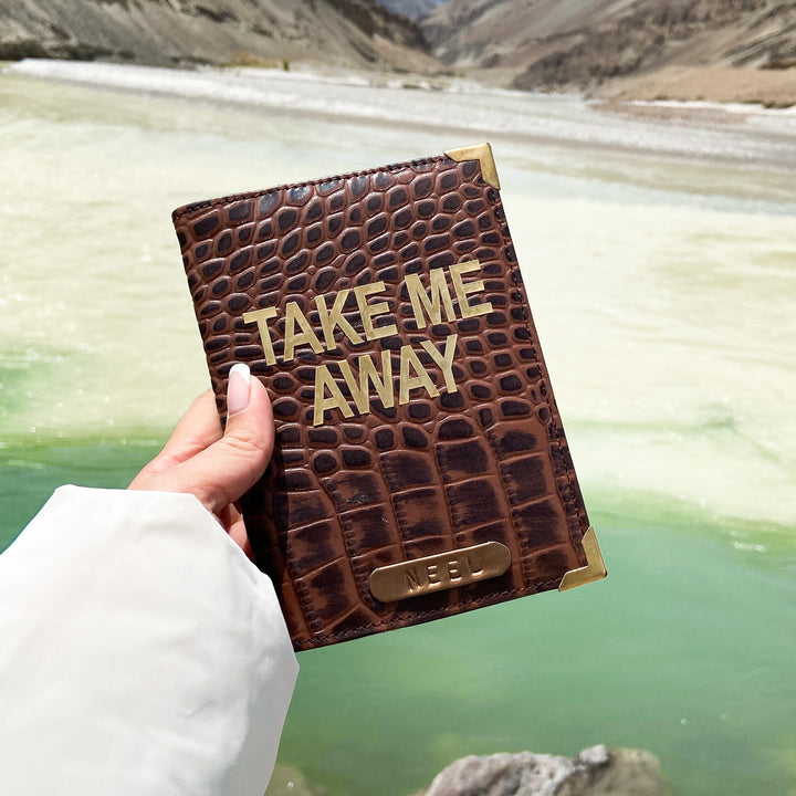 A hand holding a dark brown crocodile pattern genuine leather passport cover with the text &