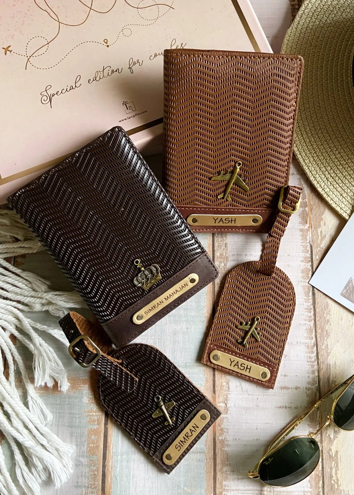 A set of couple passport covers and luggage tags with a wavy texture design in light brown and dark brown colors, displayed alongside travel-related items like a hat and sunglasses hand with the word 'YASH' embossed on it, against a backdrop of a passport, visa, and sunglasses -TPC Gifts