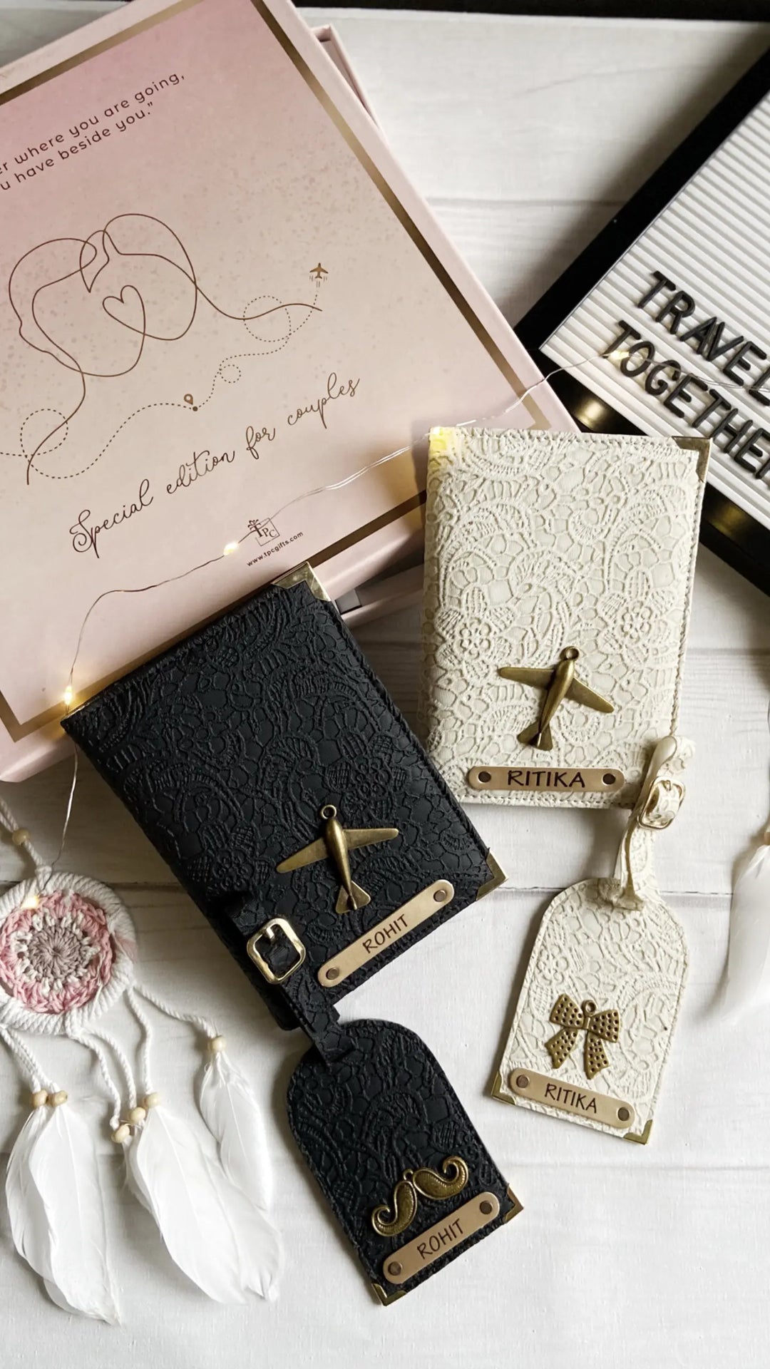 Two passport covers and two luggage tags with personalized engravings, one in black and one in a pastel color, displayed on a table with a pink gift box and a note reading &