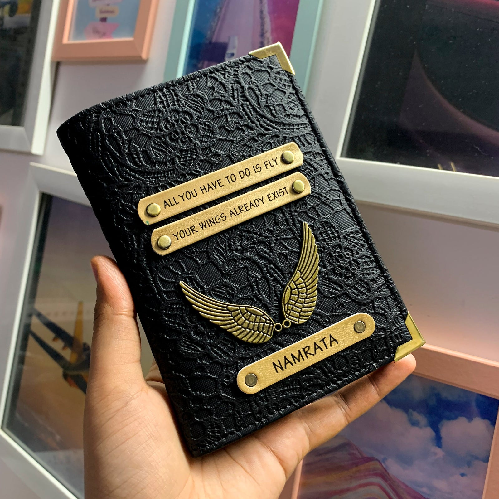 A personalized passport cover in black with gold embossed text and a metallic name plate holding a passport, displayed in a person's hand.