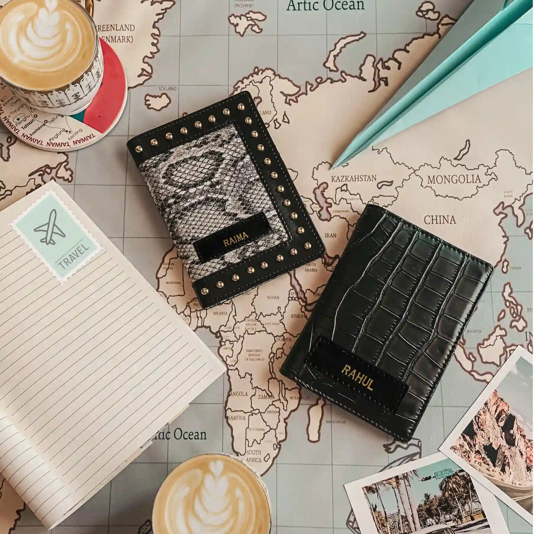 Personalised Animal Print With Stud Work &amp; Croc Black Couple Passport Cover styled on a vintage world map background. One has a snakeskin pattern with gold studs and the other has an embossed crocodile texture, both with black nameplates  -TPC Gifts