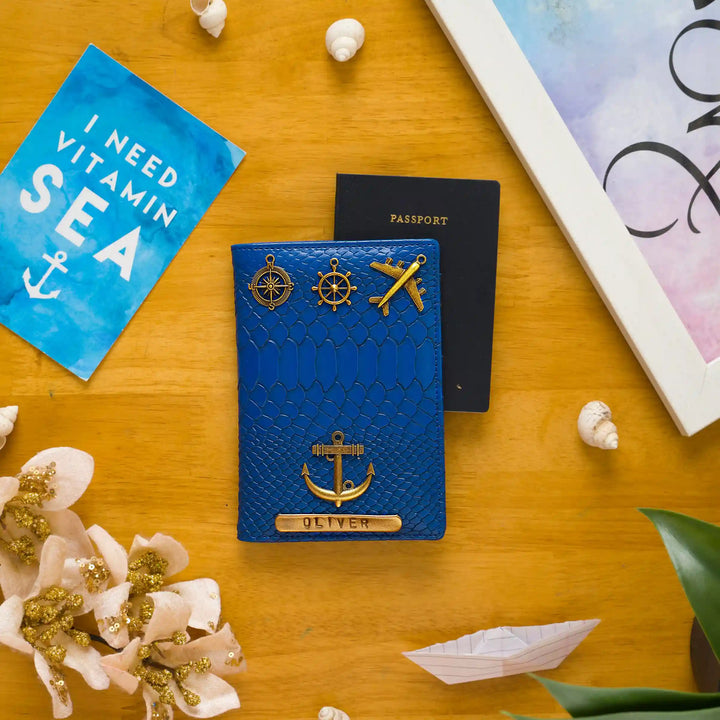 A textured blue passport cover with gold nautical-themed pins and an engraved nameplate reading &