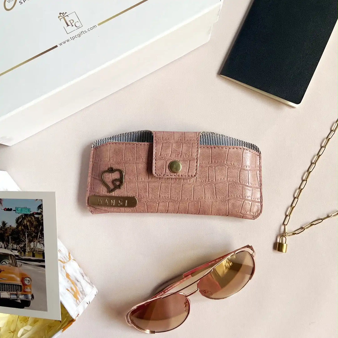 A onion crocodile texture sunglass cover displayed alongside a passport, a book, and a pair of sunglasses on a light-colored surface -TPC Gifts