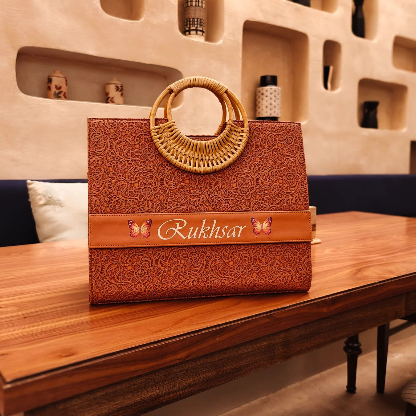 A brown personalized tote bag by TPC Gifts with a cane handle, sitting on a wooden table, with a brand name visible on the side.