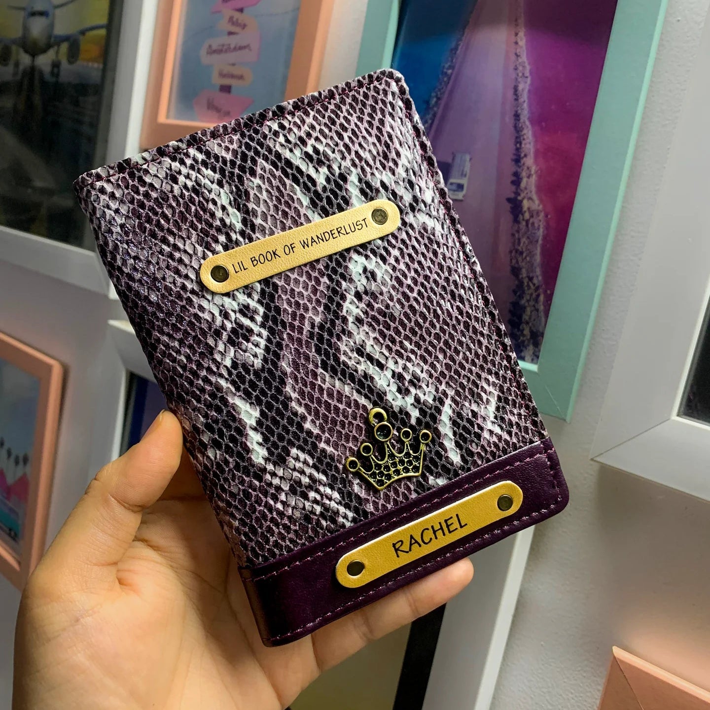 A personalized passport cover in purple with a name tag displaying the name Rachel, held in a hand.