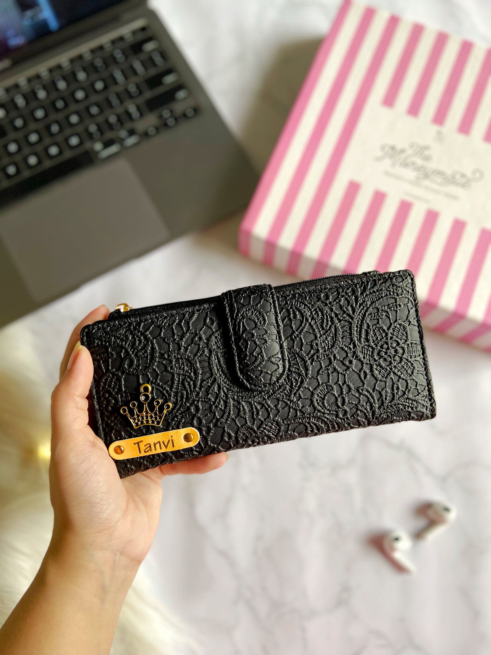 A hand holding a black textured wallet with a decorative edge and a label that reads 'Glided Grace - TPC'.