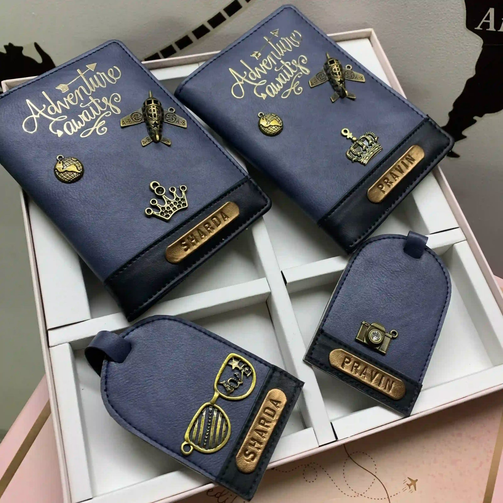 A set of personalized passport covers and luggage tags displayed in a white box with blue shading, featuring gold bronze motifs and customized text with couple edition box by tpc gifts 