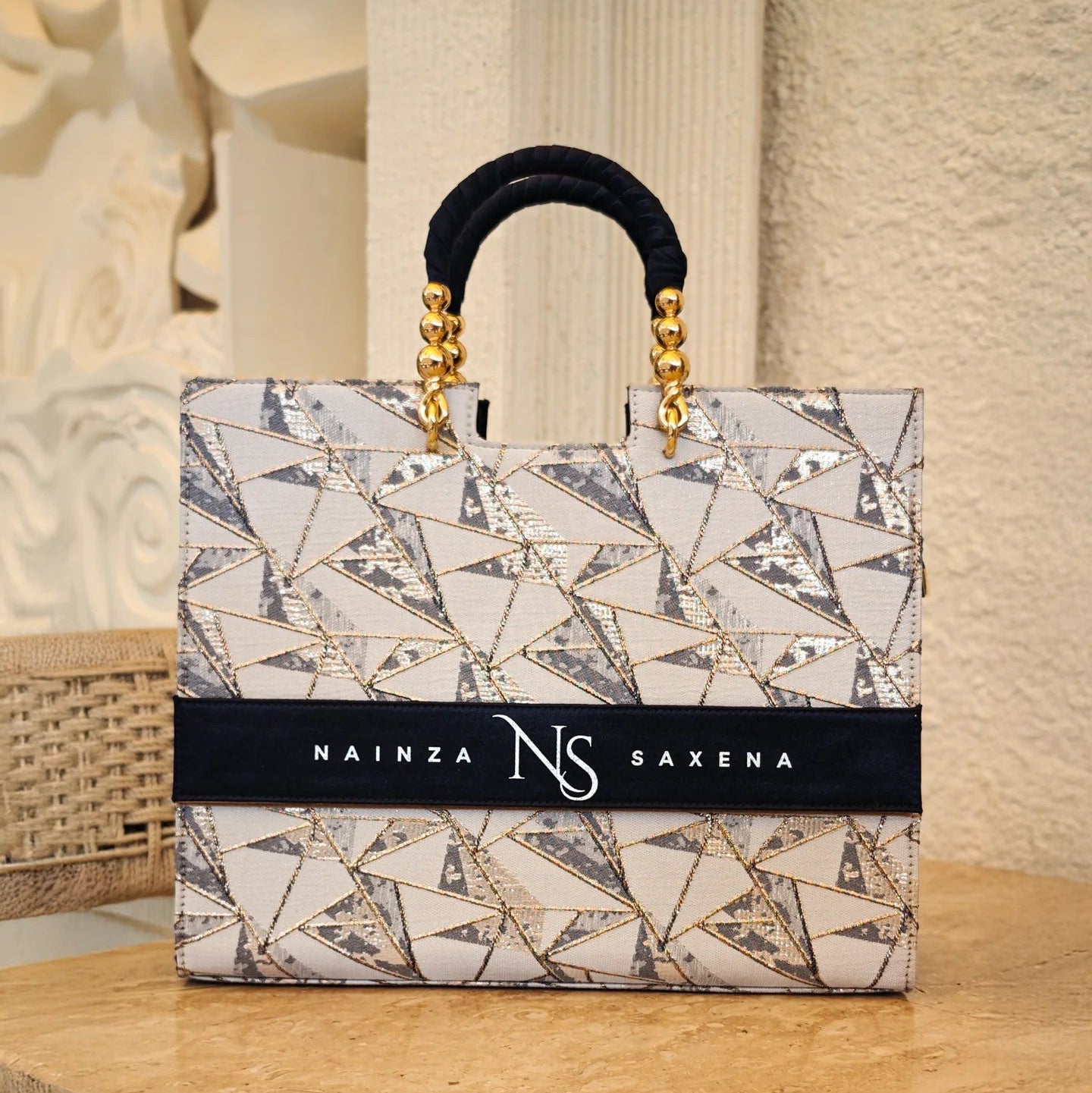 A luxurious Royal Jewel navy blue tote bag by TPC Gifts with gold-plated handle, displayed on a wooden surface, featuring a geometric pattern and brand logo.