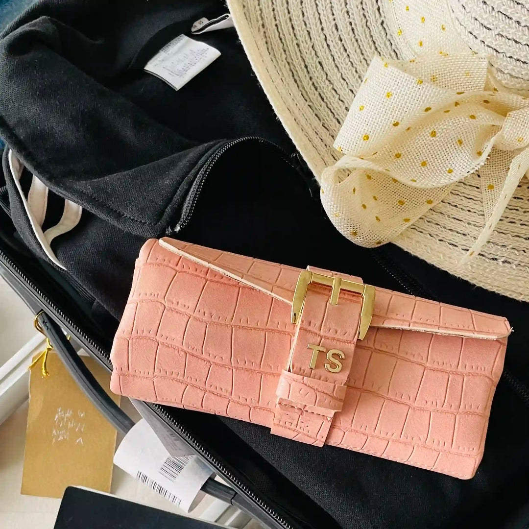 A pink crocodile-embossed clutch wallet with a gold buckle and &