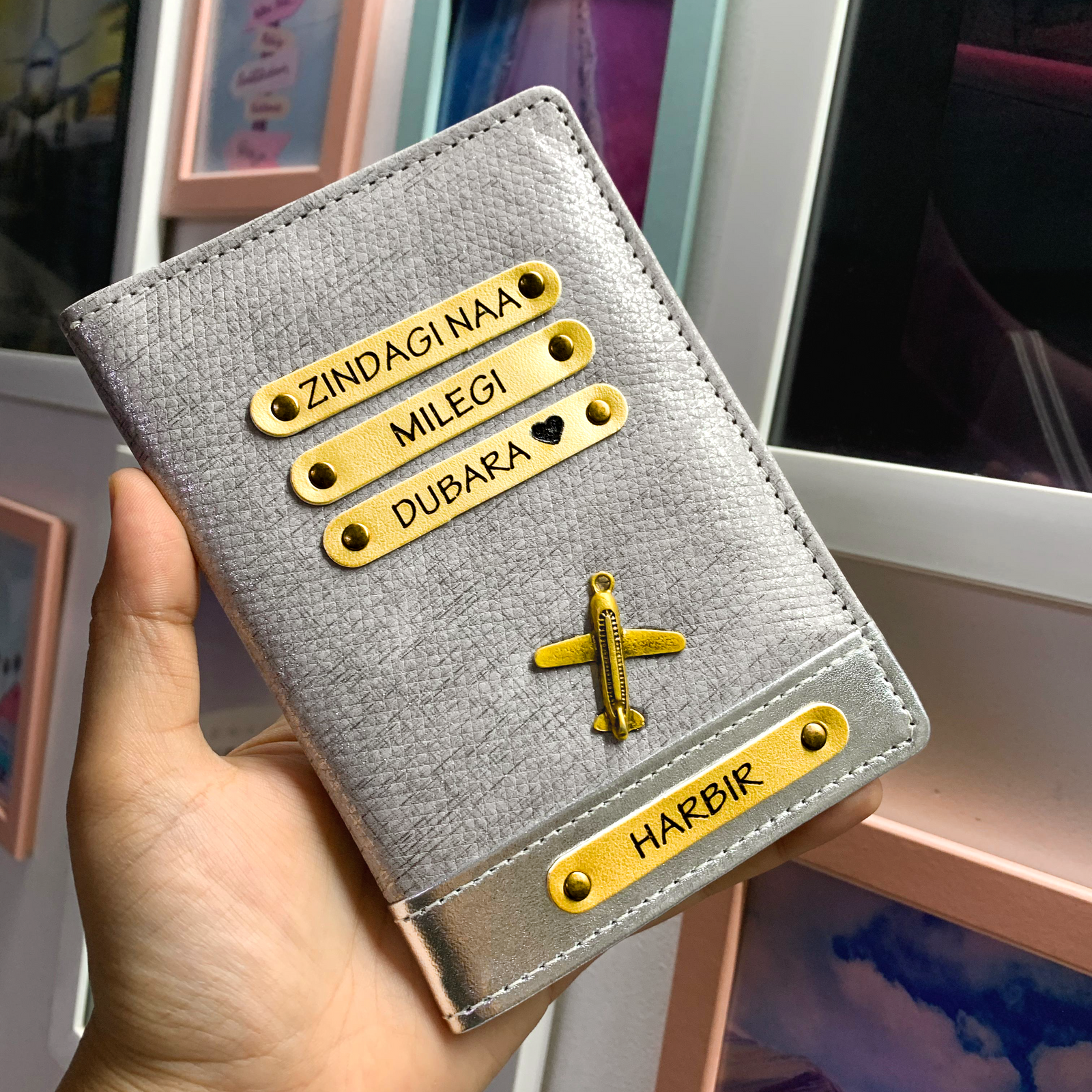 A personalized passport cover held in hand, featuring a shiny silver texture with personalized name tags and a charm.