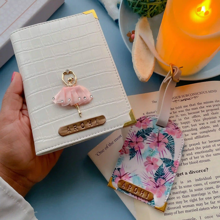 White Croco Passport Cover &amp; Tropical Luggage Tag.A styled flat-lay featuring a white crocodile-embossed passport cover with a pink doll charm and a matching floral luggage tag alongside candel and a book -TPC Gifts