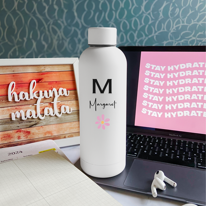 Custom engraved white stainless steel water bottle with a personalized message displayed on a desk, alongside a laptop and other items.