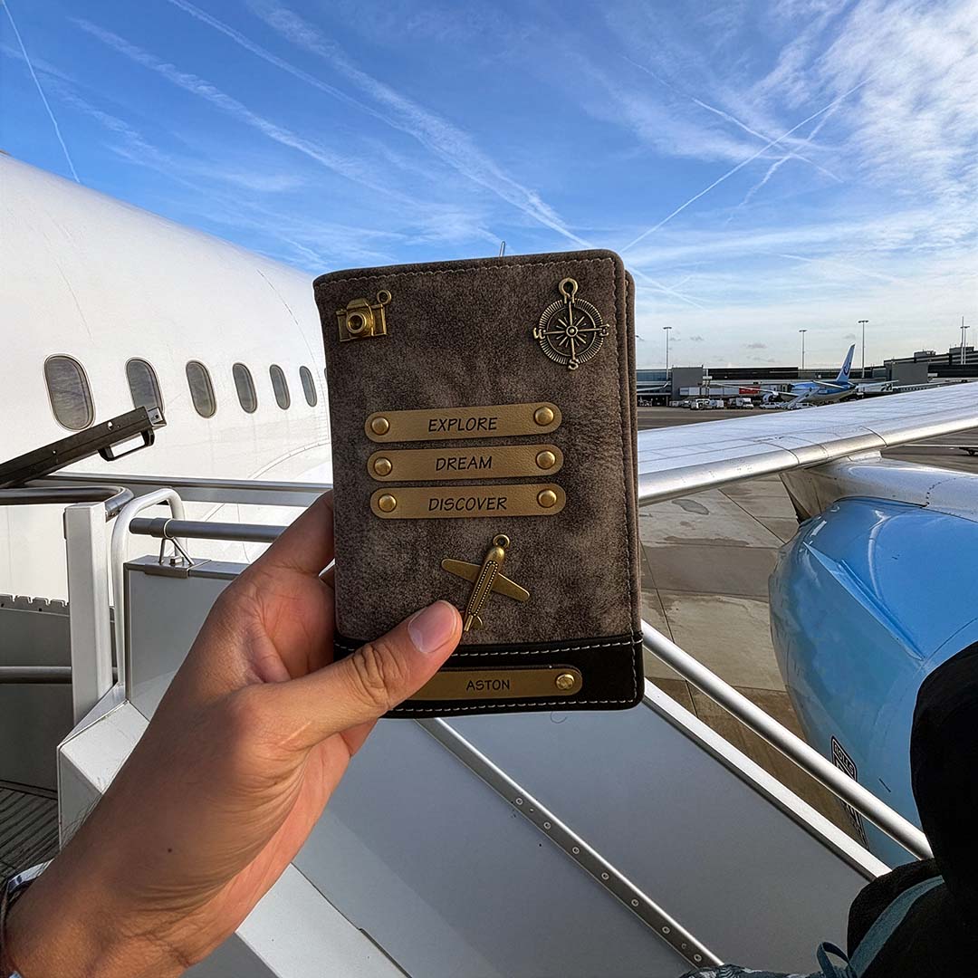 Hand holding a leather passport holder with airplane wing and blue sky in the background