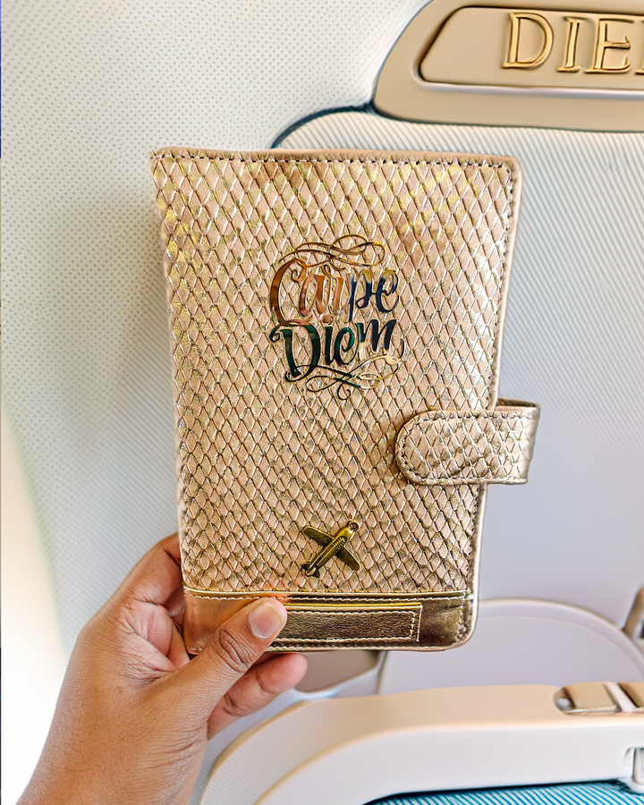A person holding a rose gold travel wallet by TPC Gifts with a designer exterior, showing a personalized name tag and an airplane window in the background.